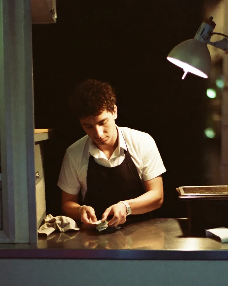 An operator counting cash on the steel counter of a closed food truck under one work light, late at night.
